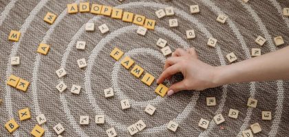 A hand arranges letter tiles spelling 'family' and 'adoption' on a circular patterned carpet.