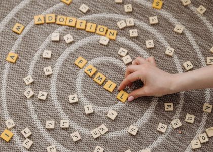A hand arranges letter tiles spelling 'family' and 'adoption' on a circular patterned carpet.