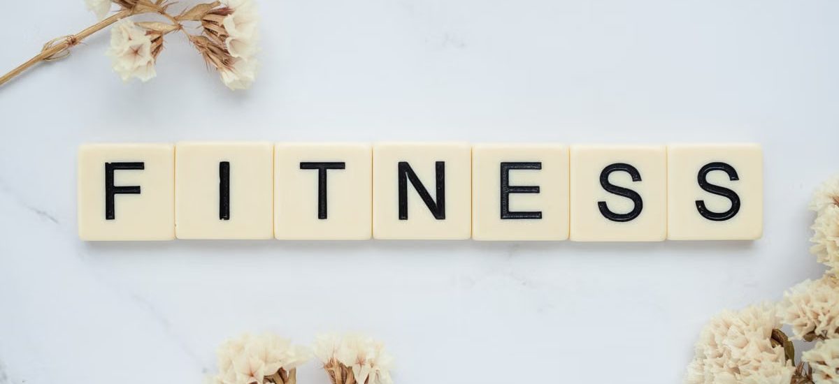 Close-up of scrabble tiles spelling 'FITNESS' on a marble surface with white flowers.