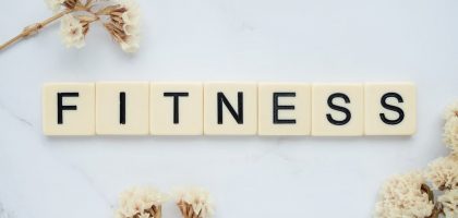Close-up of scrabble tiles spelling 'FITNESS' on a marble surface with white flowers.